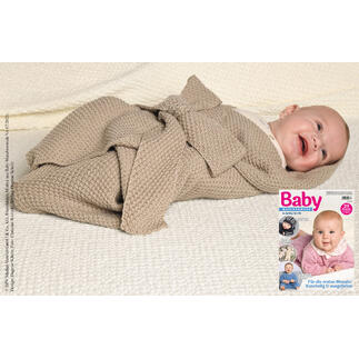 Lächelndes Baby in einem Pucktuch aus Nuovo Merino auf einem weißen Strickstück