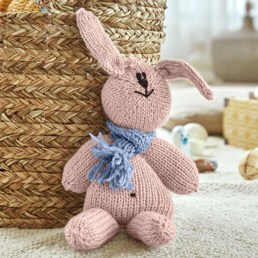 Hasi, ein gestricktes Kuscheltier mit Schal, sitzt vor einem geflochtenen Korb.