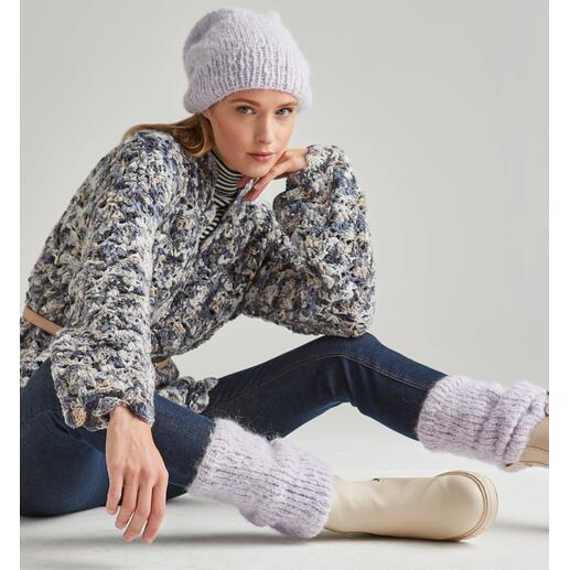 Frau in gestrickter Mütze und Beinstulpen sitzt elegant auf dem Boden.