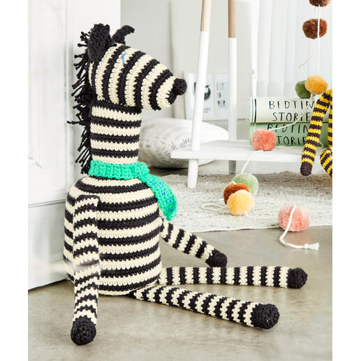 Häkelzebra ‚Zack‘ aus Cotonara, sitzend mit türkisfarbener Schärpe.