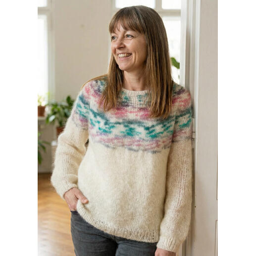 Frau in einem hellen Pullover mit buntem Muster, lächelt vor einem Fenster.