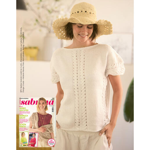 Frau trägt weißen Pulli aus Cottonprima, steht mit Strohhut im Hintergrund.