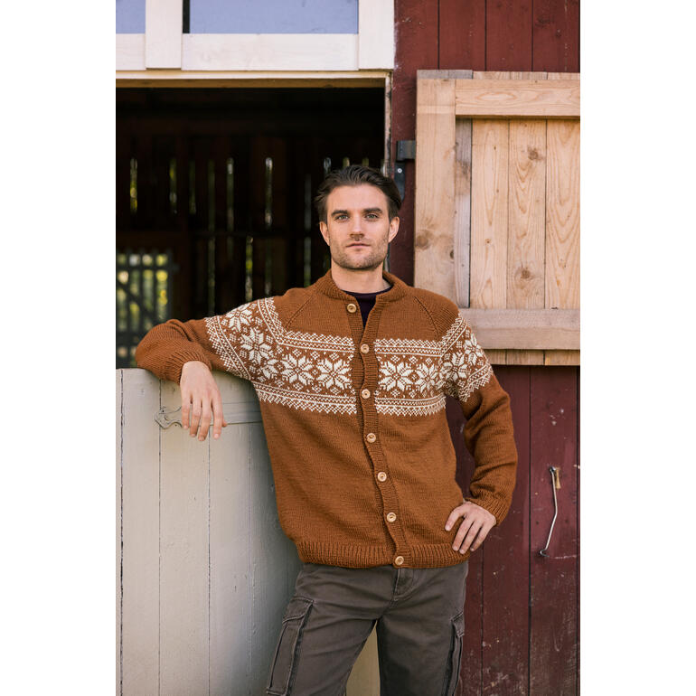 Mann lehnt an einer Wand, trägt einen braunen Cardigan mit gestricktem Muster und schaut in die Kamera.