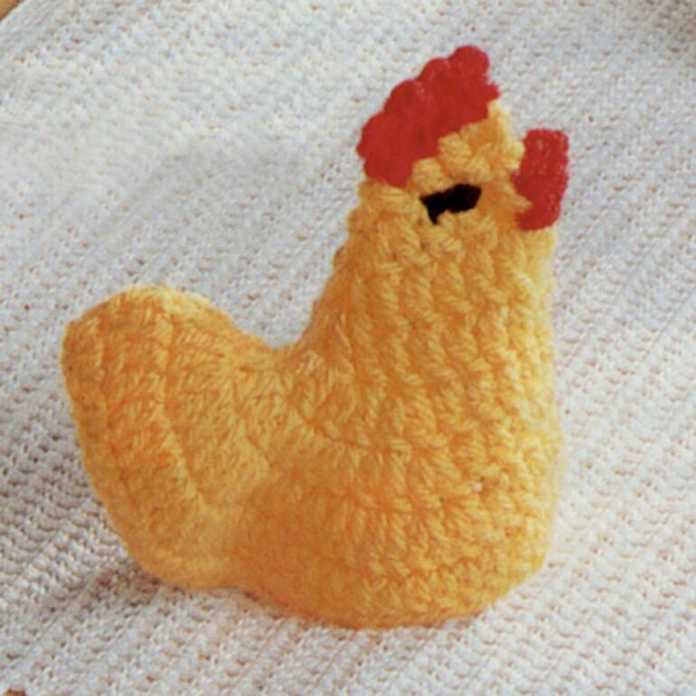 Gehäkeltes gelbes Küken mit rotem Kamm, vor einem weißen Hintergrund.