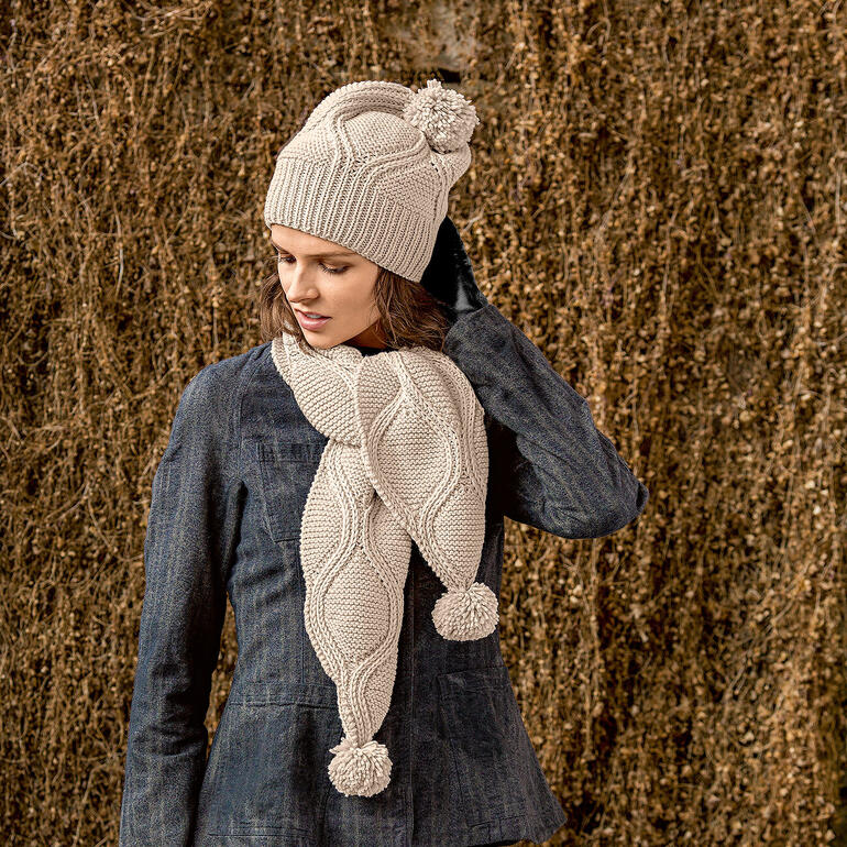 Frau trägt eine helle Mütze und einen Schal mit Bommel aus Merino+.