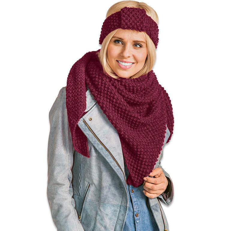 Frau in grauem Outfit trägt ein rotes Tuch und ein passendes Stirnband, lächelt in die Kamera.