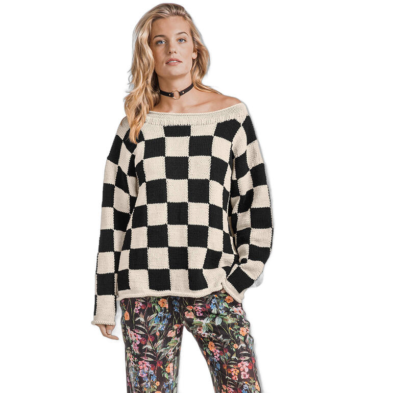 Frau trägt einen schwarzen und cremefarbenen Pullover mit Karomuster, kombiniert mit blühenden Hosen.
