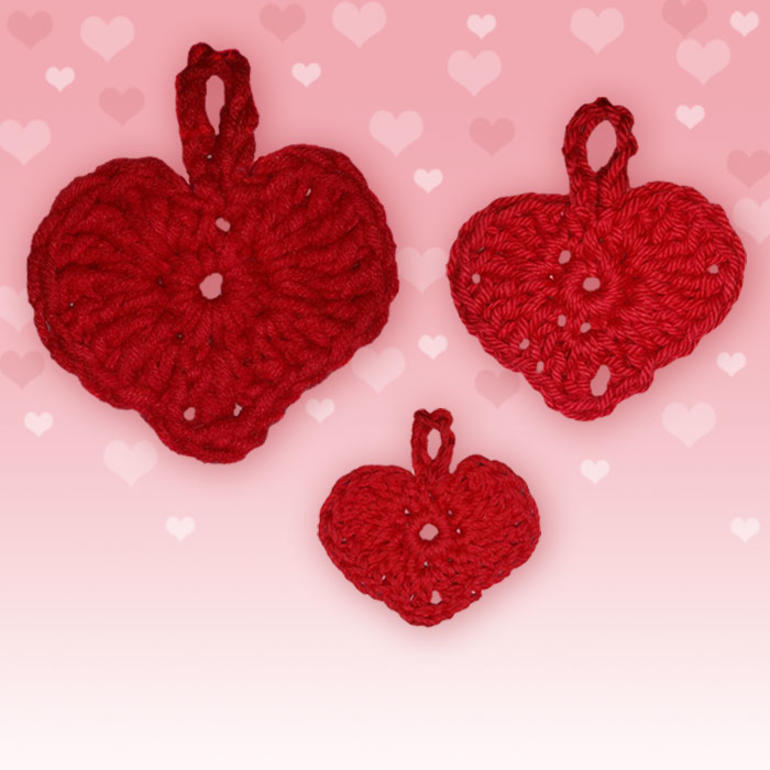 Drei rote gehäkelte Herzen in unterschiedlichen Größen auf rosa Hintergrund.