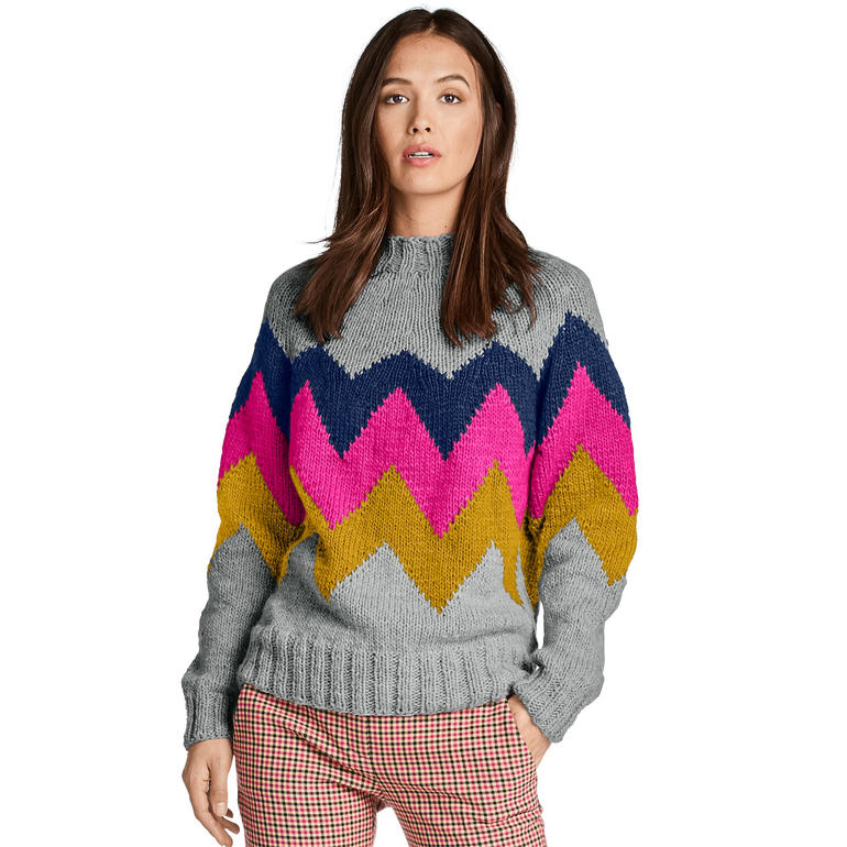 Frau in grauem Pullover mit bunten Zickzack-Muster, blickt in die Kamera.
