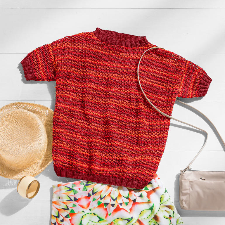 Gestreifter roter Damenpulli mit kurzen Ärmeln, neben einer Strohhut.
