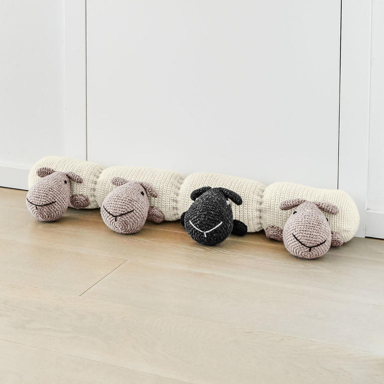 Zugluftstopper mit Schäfchen-Motiv, auf den Boden vor einer Tür platziert.