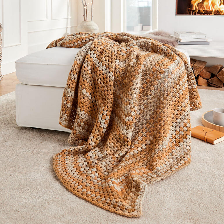 Gehäkelte Decke aus Cassandra Print in warmen Farbtönen auf einem Sofa.