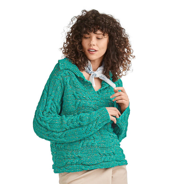 Frau trägt einen grünen Pullover aus Oletta, posiert vor neutralem Hintergrund.