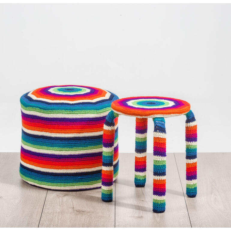 Bunter Hockerbezug und Sitzpouf aus Poco stehen in einem hellen Raum.