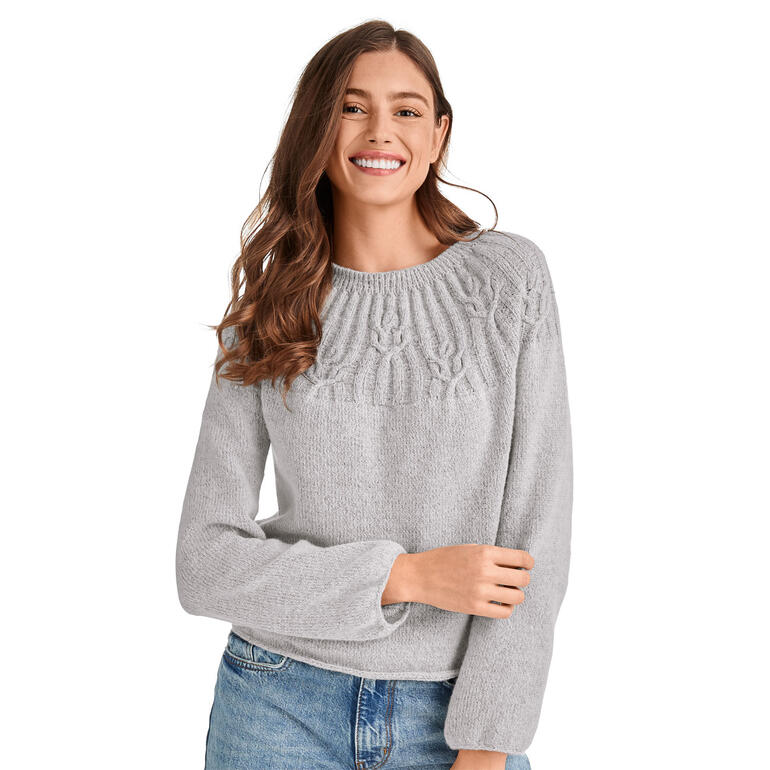 Hellgrauer Pullover aus Charme®, getragen von einer Frau mit lockigen Haaren.