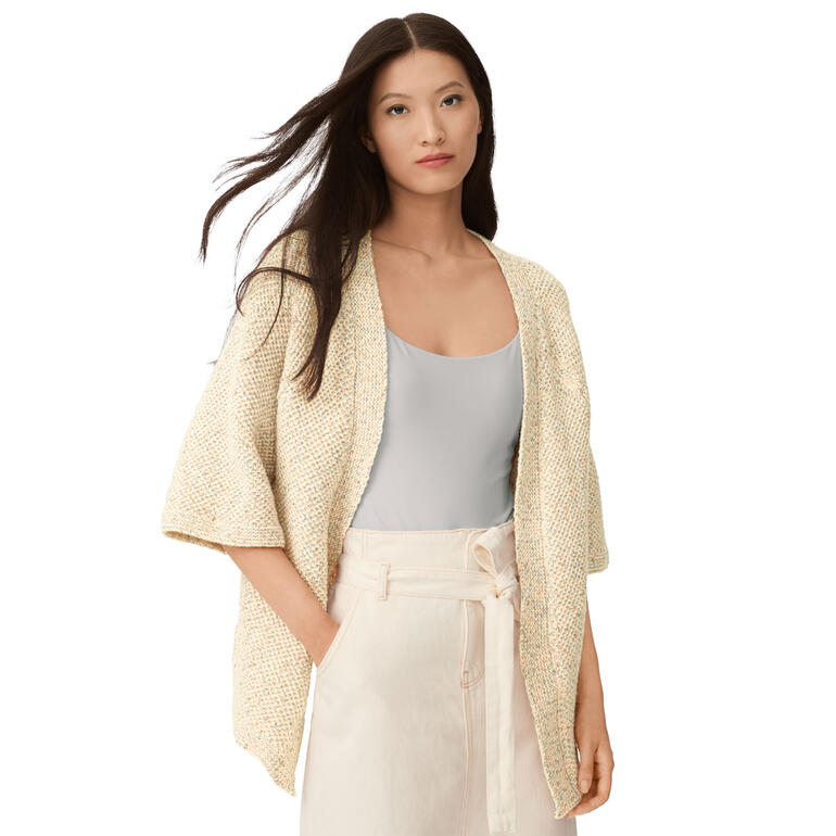 Frau in beiger Kimono-Jacke mit lockerer Passform vor weißem Hintergrund.