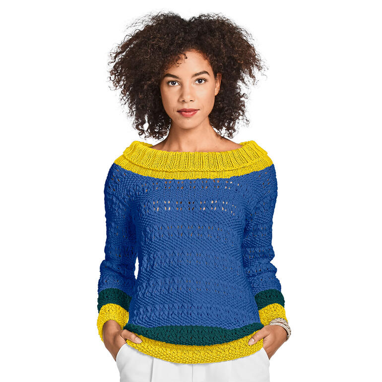 Frau in blau-gelbem Pullover aus Cotonara steht mit einer Hand in der Hüfte.