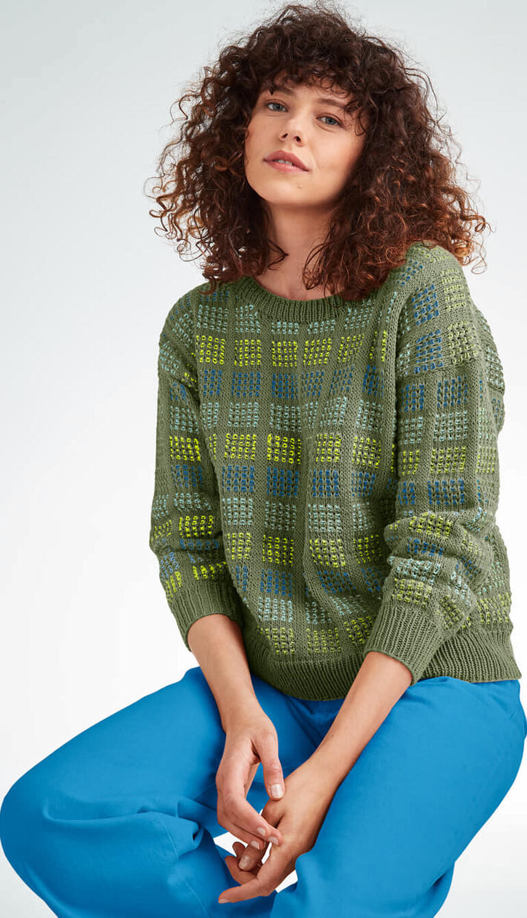 Grüner Pullover aus Cotonia II mit Mustern, Frau mit lockigen Haaren sitzt.