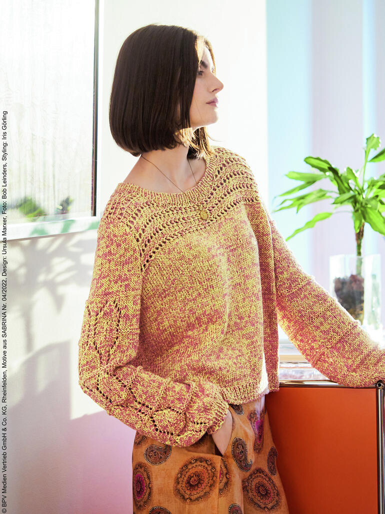 Frau in einem gelben Oversized-Pulli mit langen Ärmeln am Fenster