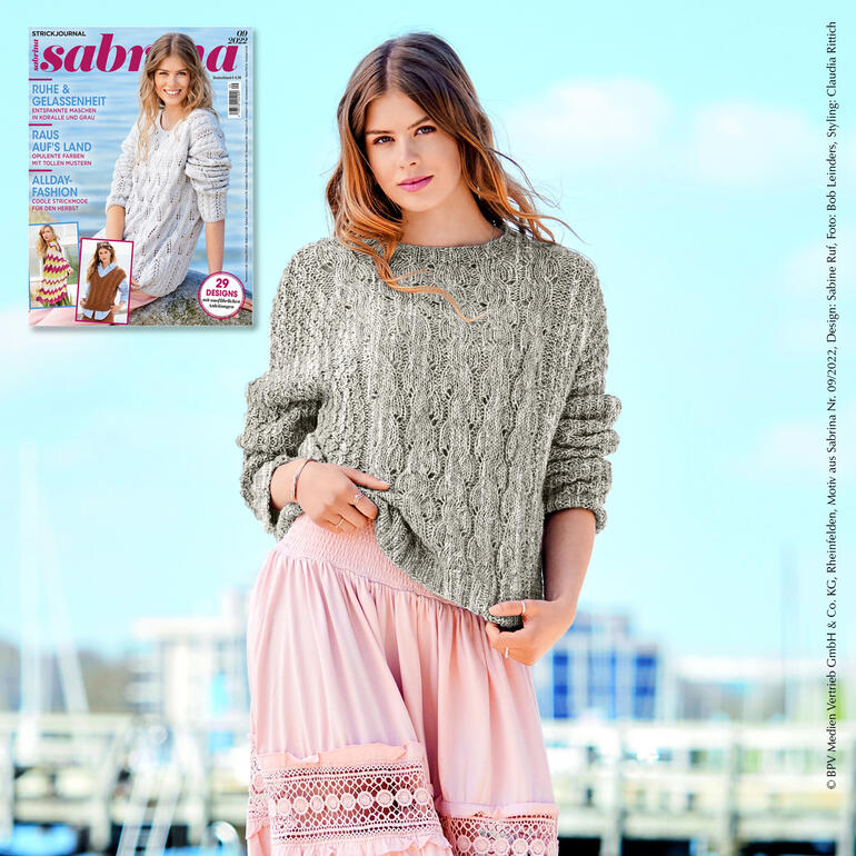 Frau in Oversized-Pullover aus Wool-Cotton steht vor einem Magazinhintergrund.