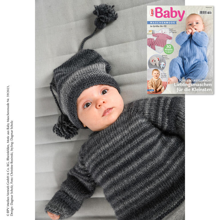 Babe in grauem Babypullover mit Mütze auf einer Decke.