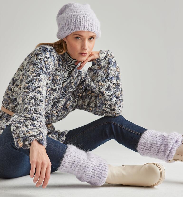 Frau in gestrickter Mütze und Beinstulpen sitzt elegant auf dem Boden.