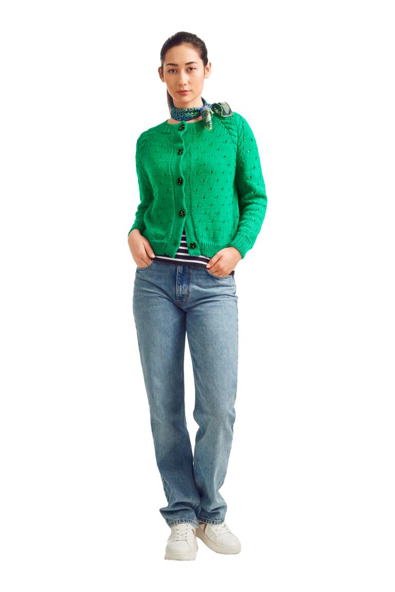 Frau in grüner Jacke mit gepunktetem Muster steht in lässiger Pose.