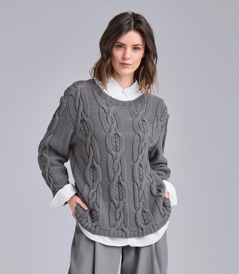 Grauer Pullover mit Zopfmuster und weitem Schnitt, vor grauem Hintergrund.