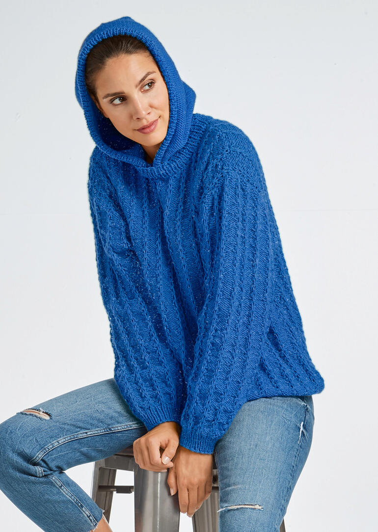 Blauer Kapuzenpullover aus Merino-Classic, sitzende Frau mit entspanntem Lächeln.