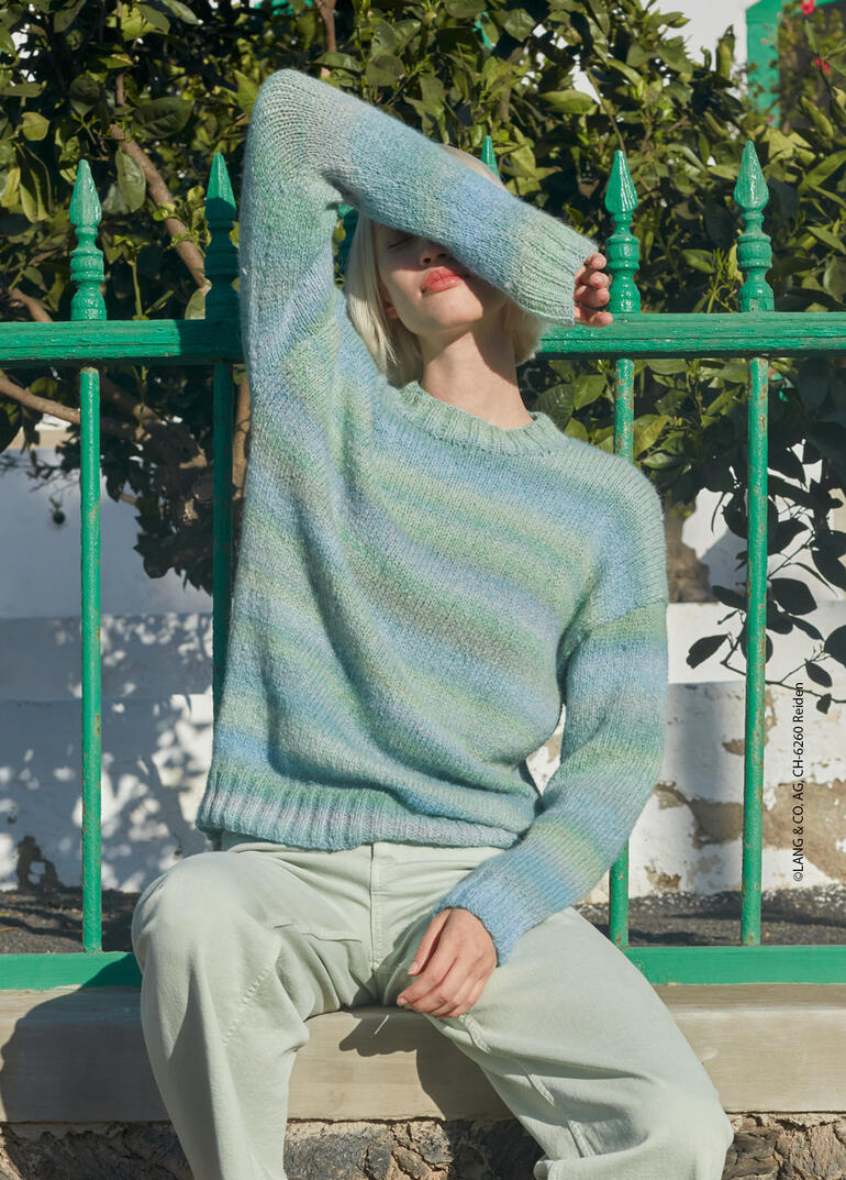 Frau in pastelgrünem Pullover sitzt entspannt vor einer grünen Wand.