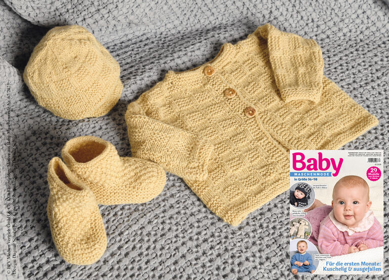 Gelbe Babyjacke, Mütze und Söckchen auf einem grauen Strickstück