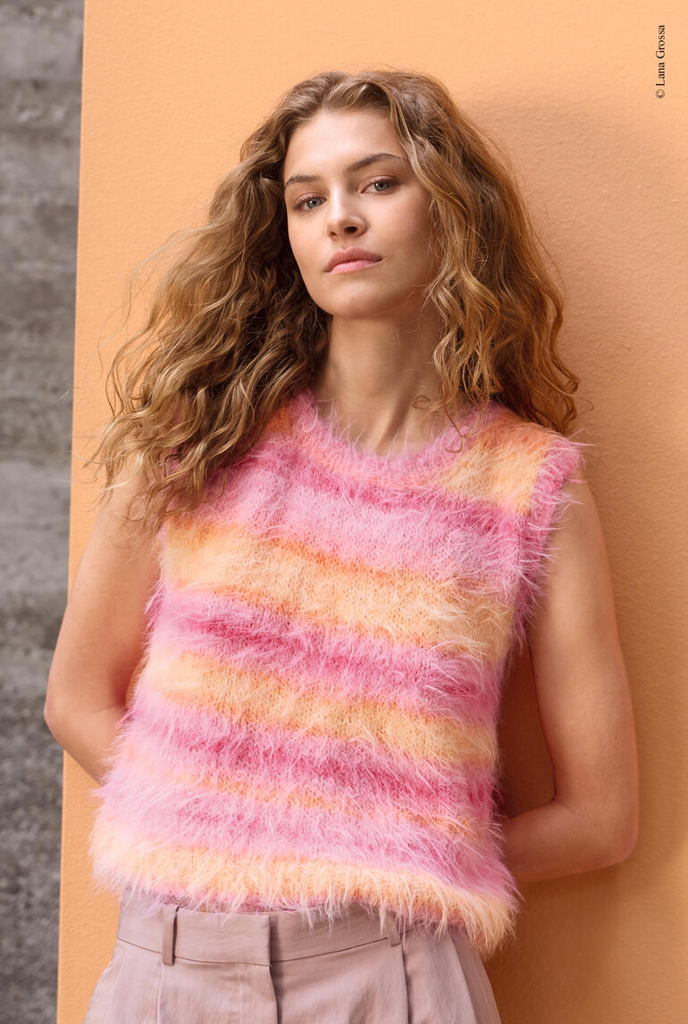 Frau in rosa-orange gestreiftem Top aus Basta Mista posiert vor einer bunten Wand.