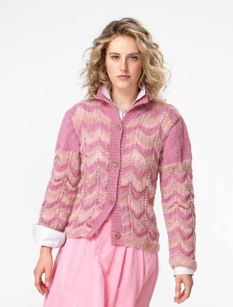 Frau steht in einer rosa Jacke mit Zopfmuster aus Landwolle.