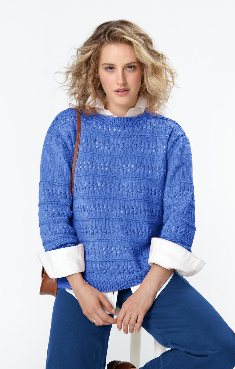 Blauer Pullover aus Merino-Wolle, getragen von einer Frau mit lockigem Haar.