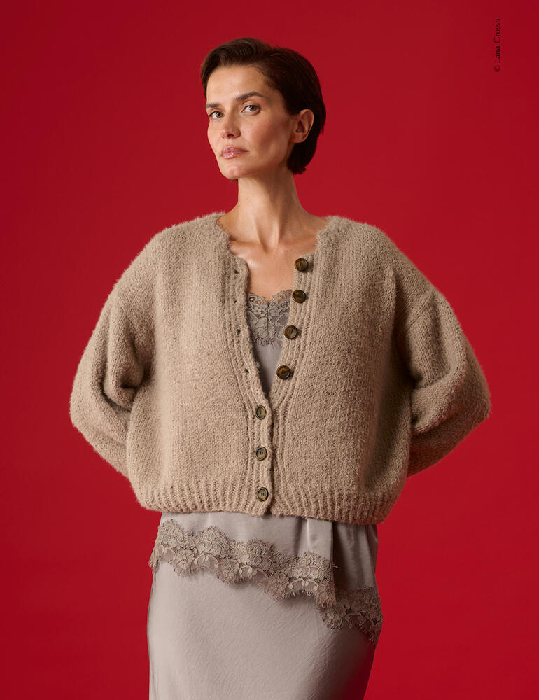 Beige Jacke aus Cosi mit Knöpfen, Modell steht vor rotem Hintergrund.