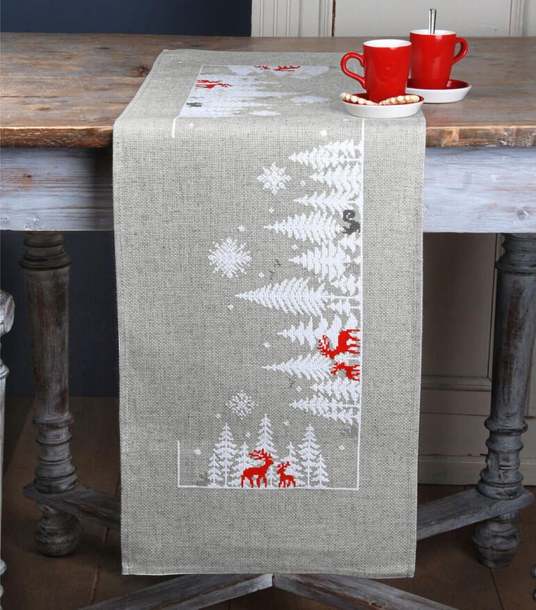 Tischläufer mit Wintermotiven, darunter Rehe und verschneite Tannenbäume.