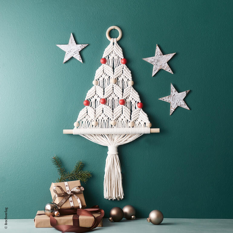 Kleiner Weihnachtsbaum aus Makramee an einer grünen Wand, umgeben von Sternen.