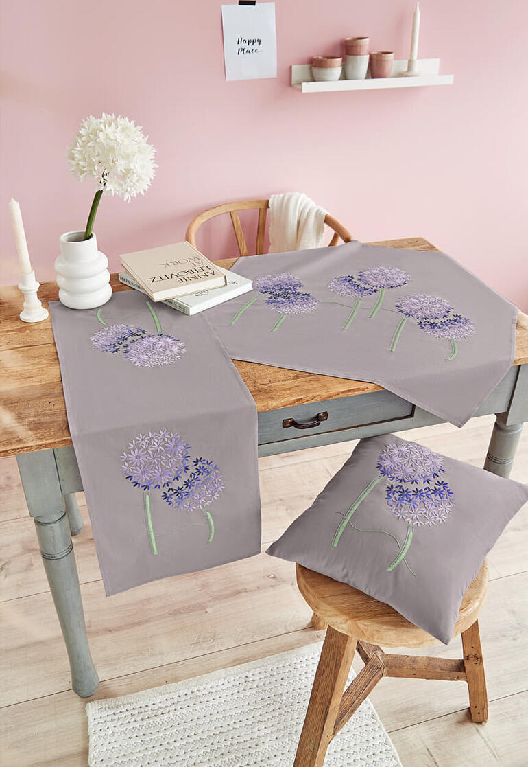 Tischset und Kissen mit lila Blumenmotiven auf einem Holztisch.