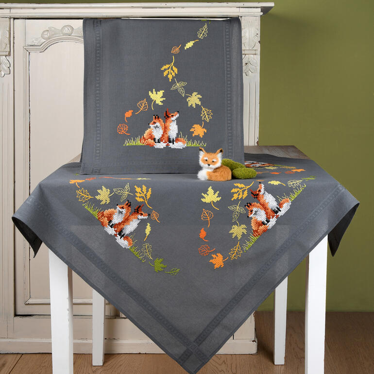 Tischwäsche-Set mit herbstlichen Füchsen auf Tisch und Stuhl.