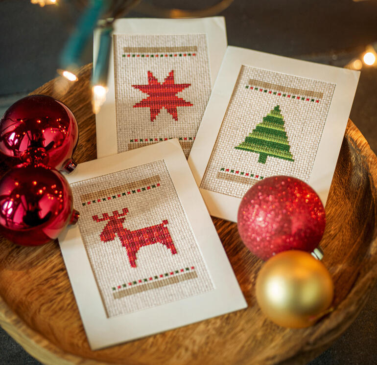 Drei Weihnachtskarten auf einem rustikalen Holztablett, umgeben von Weihnachtsdekoration.