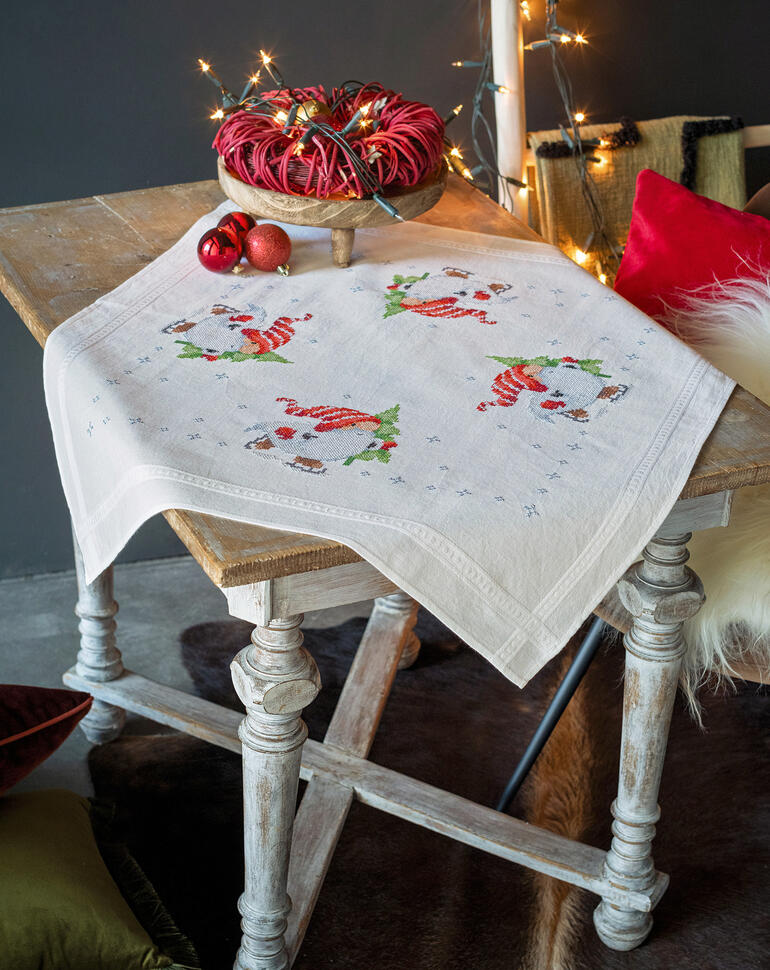 Tischdecke mit Wichteln und winterlicher Dekoration auf einem Holztisch.