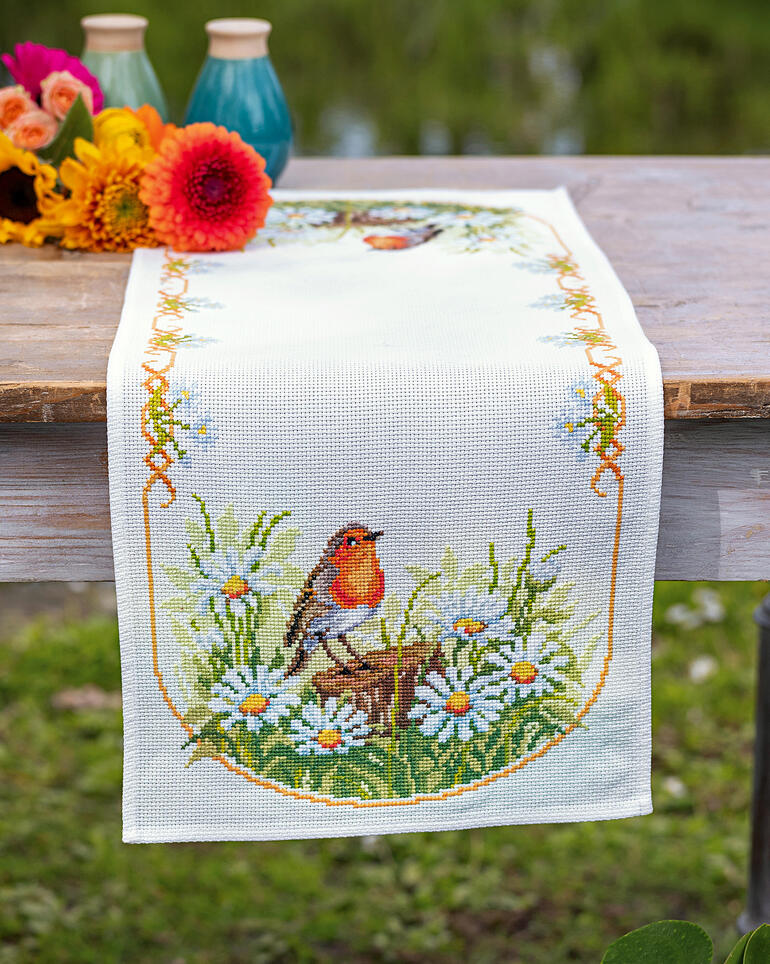 Tischläufer mit einem Rotkehlchen, umgeben von bunten Blumen auf einem Tisch.