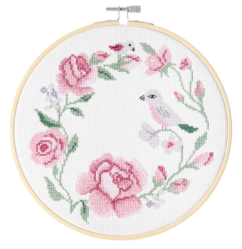 Kreuzstichbild eines Rosenkranzes mit einem kleinen Vogel auf einem weißen Stoff.