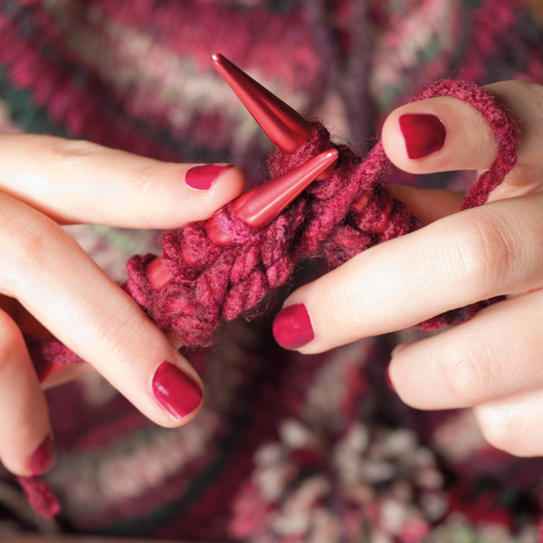 Nahaufnahme einer Frau die Stricknadeln in der Hand hat und etwas strickt